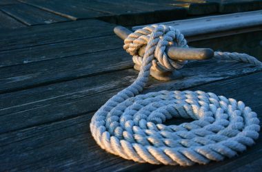 Close-up of a sturdy nautical knot on a weathered wooden dock at sunset.